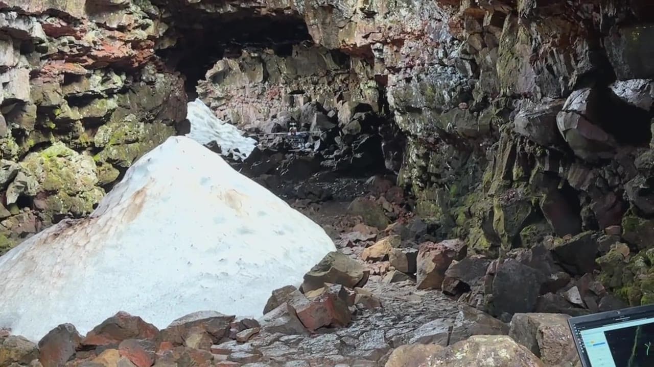 The mission drone flying autonomously inside the Iceland lava tube, past a snow cone under the entrance skylight